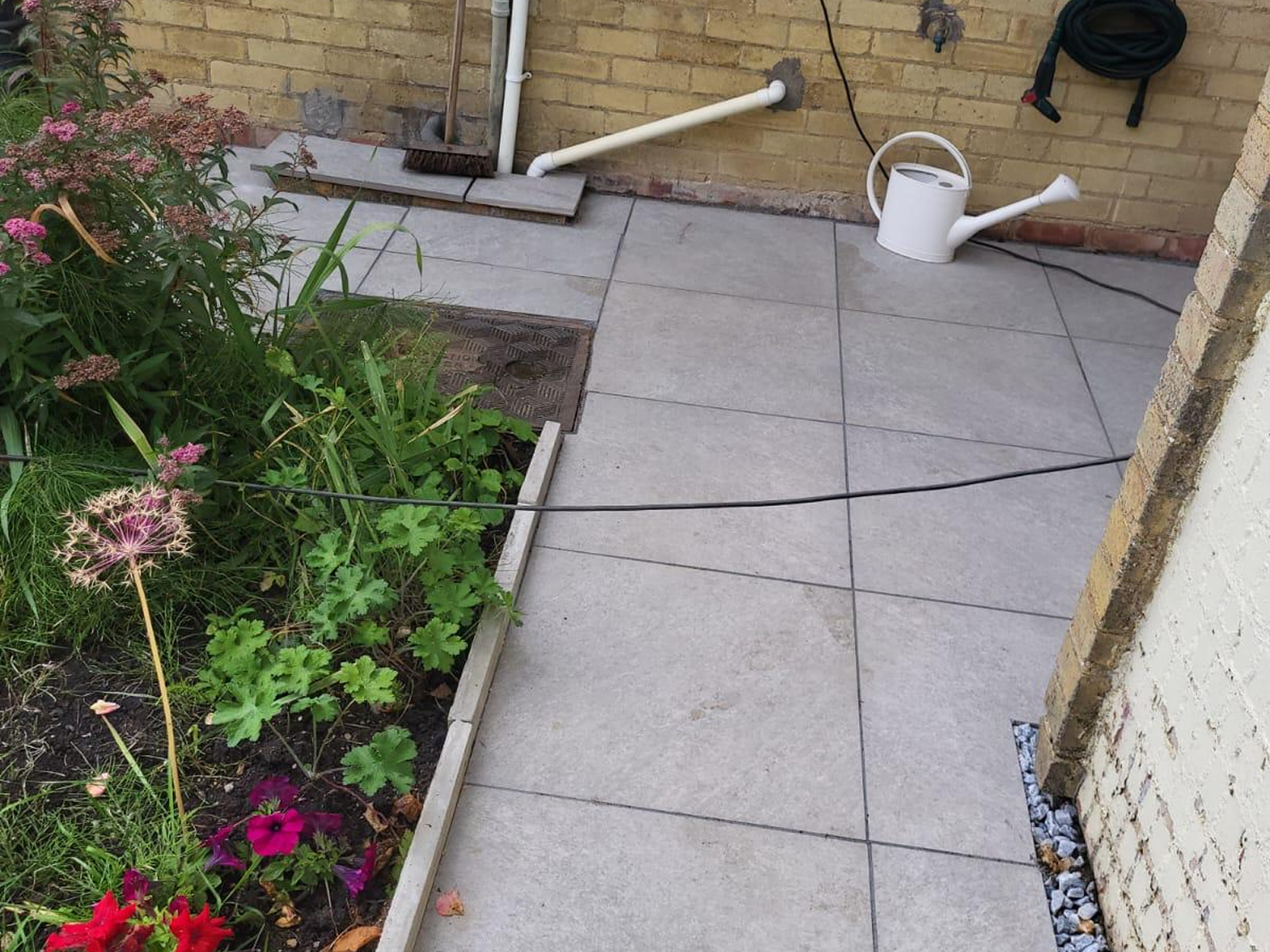 Paving image Newly installed grey garden patio paving in Aylesbury with adjacent flower bed and garden hose. High-quality patio installation by BP Fencing.